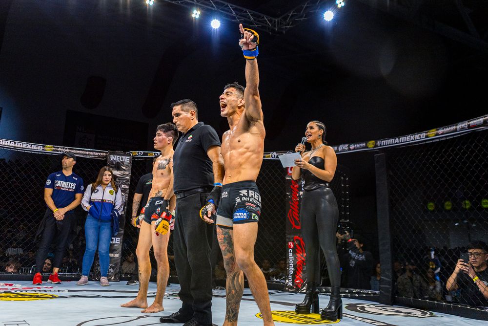 MMA fighter celebrates victory with referee raising his hand in octagon cage during professional fight event.
