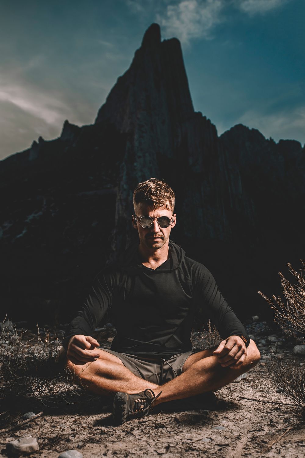 Silhouette of dramatic mountain peak with person meditating in cross-legged pose.