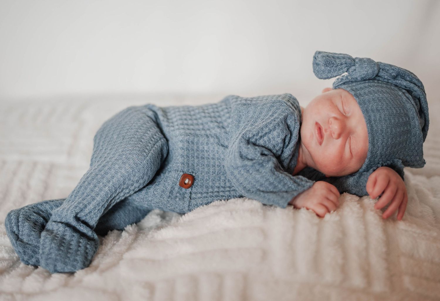 Baby wearing a cozy blue knitted outfit laying on a soft blanket.