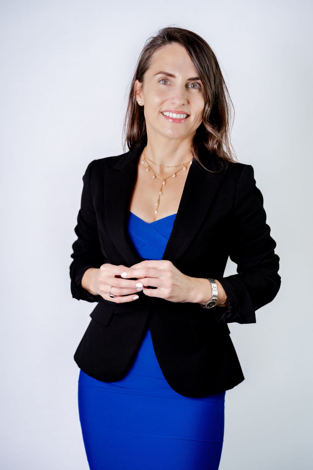Professional portrait of someone wearing a black blazer and royal blue dress against a light gray background.