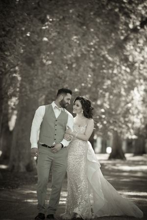 A romantic black and white photo of a couple walking through a tree-lined path in wedding attire.