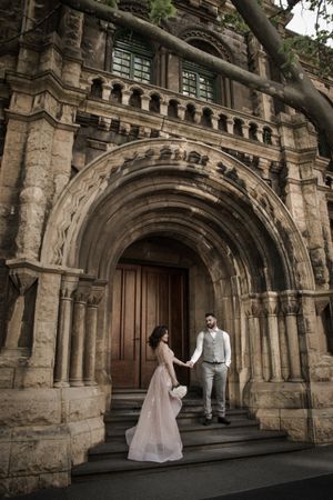 Wedding couple on stone steps of grand archway entrance to historic building.