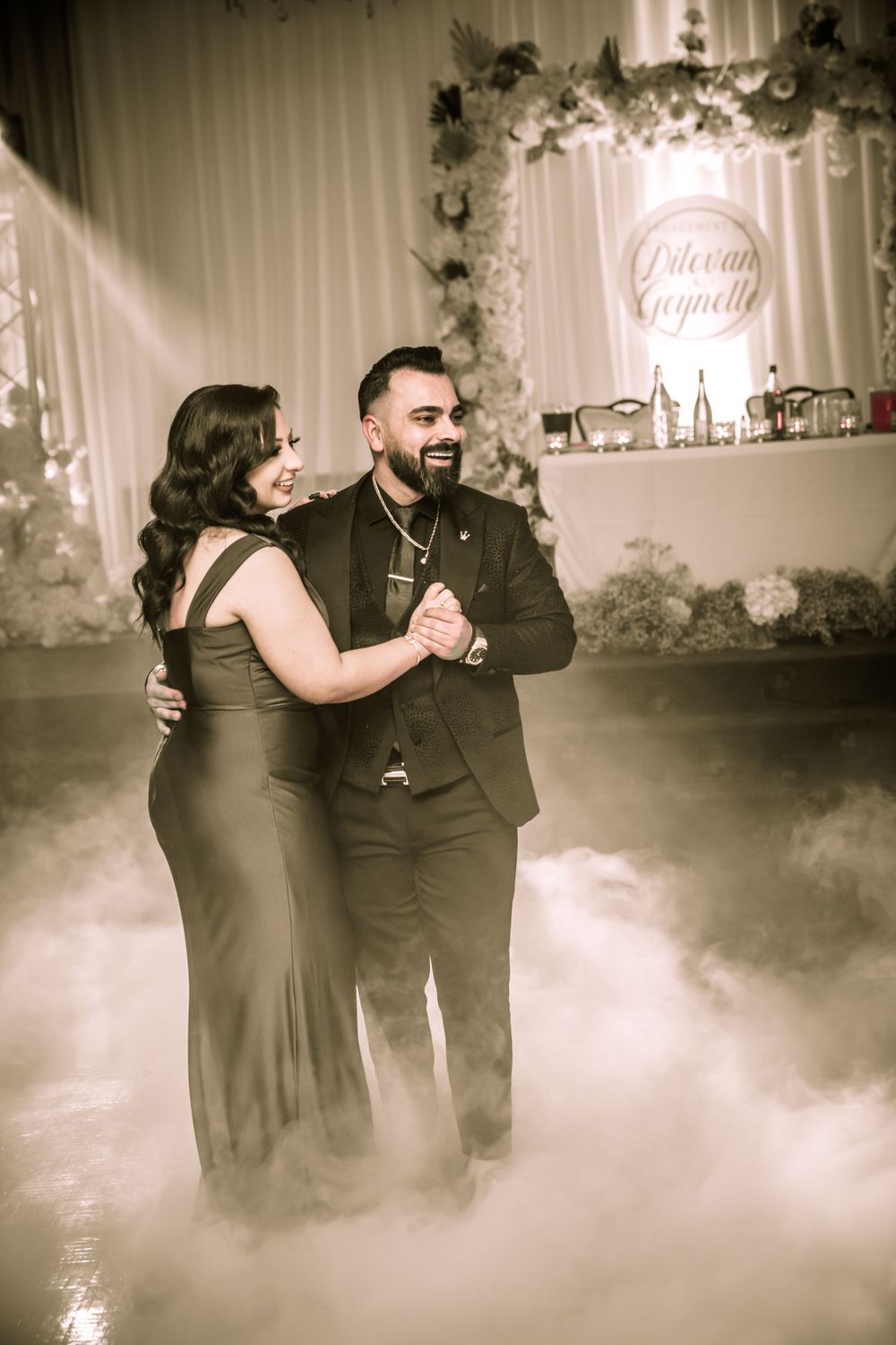 A couple dances together on a foggy dance floor with elegant floral decor and lighting.