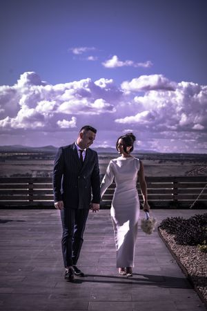 Wedding couple walking on terrace against dramatic purple sky and mountain vista.