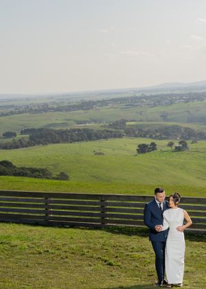 A wedding couple stands together on hillside with panoramic views of green valleys below.