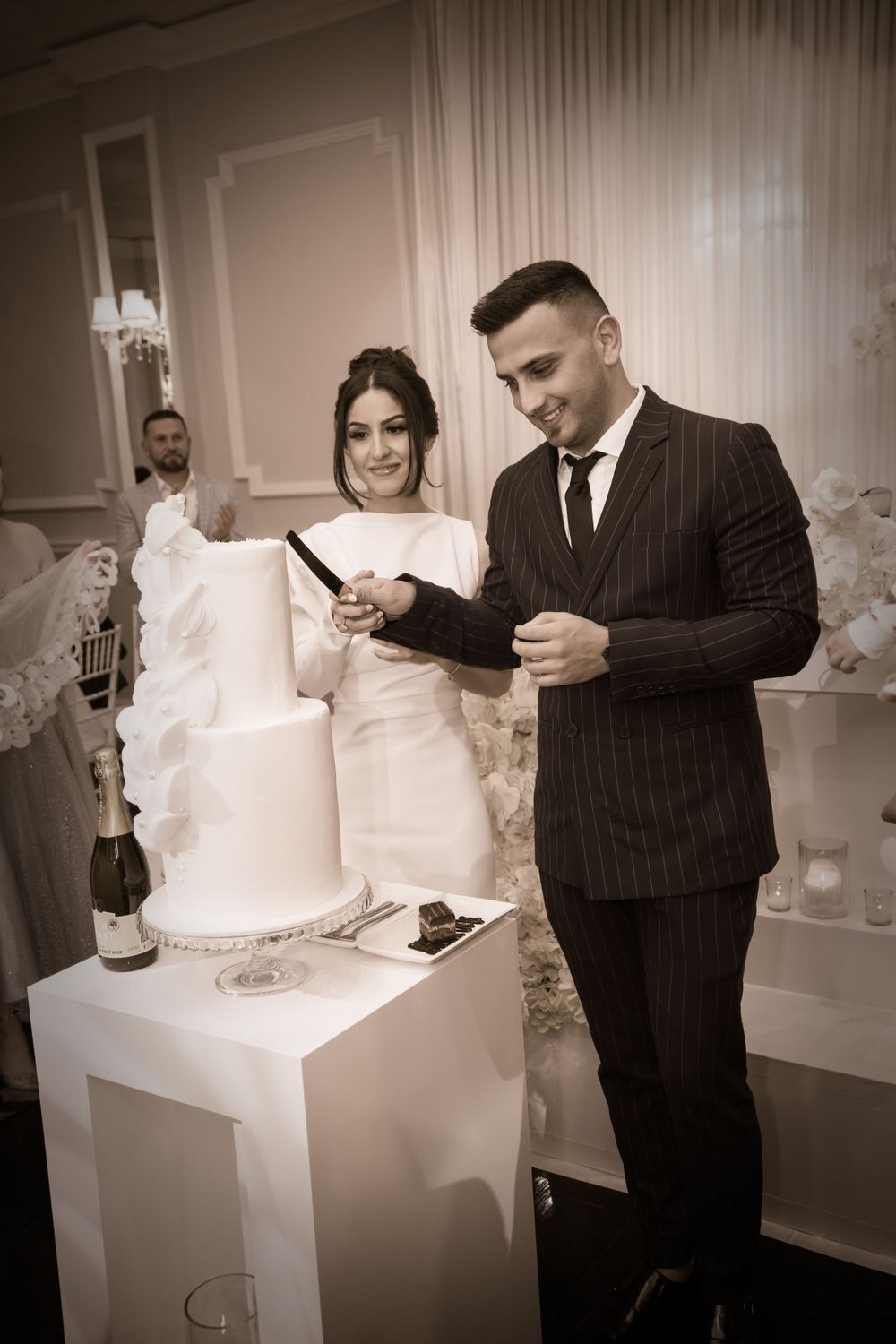 Newlywed couple cuts elegant white wedding cake during reception celebration.