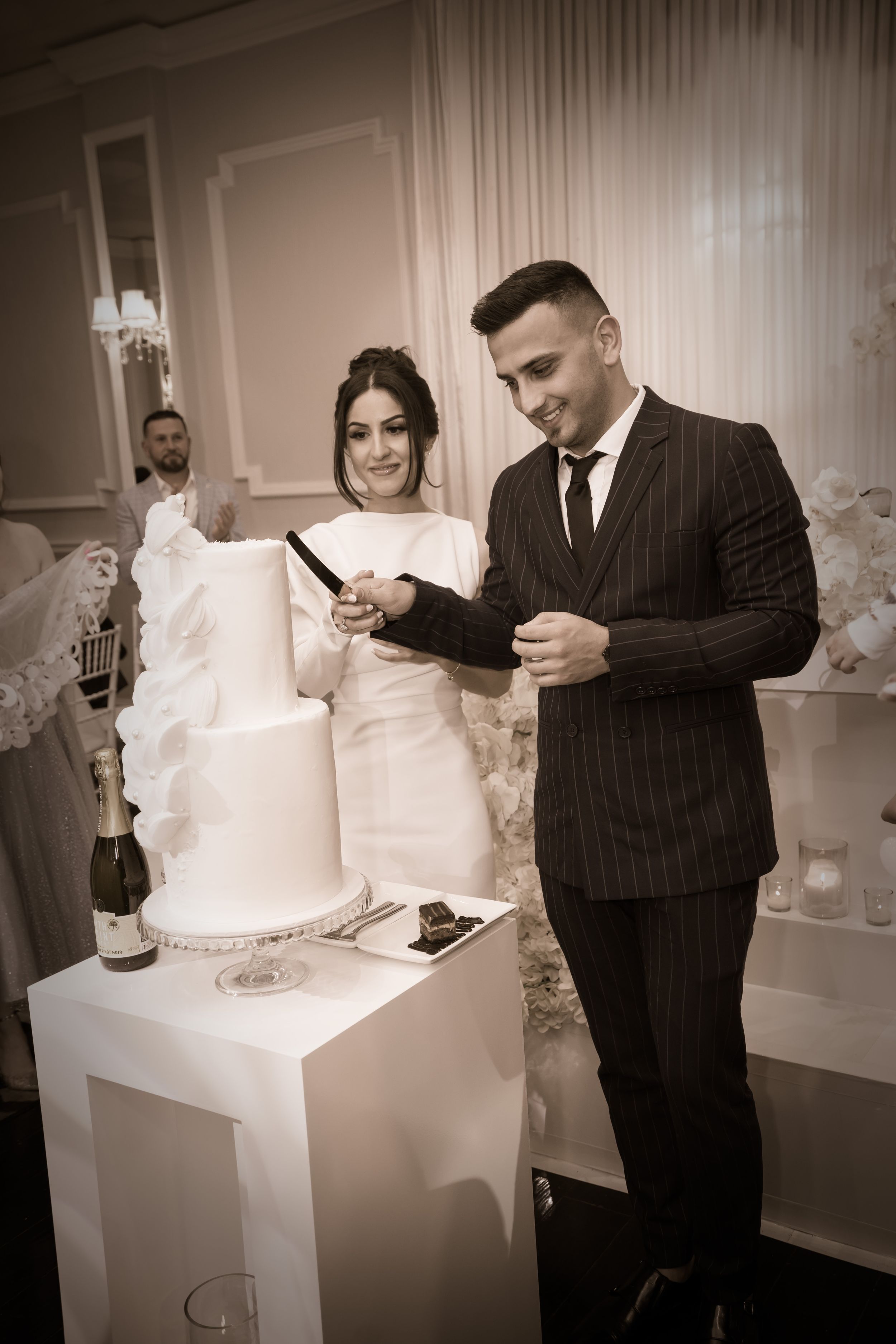 Newlywed couple cuts elegant white wedding cake during reception celebration.
