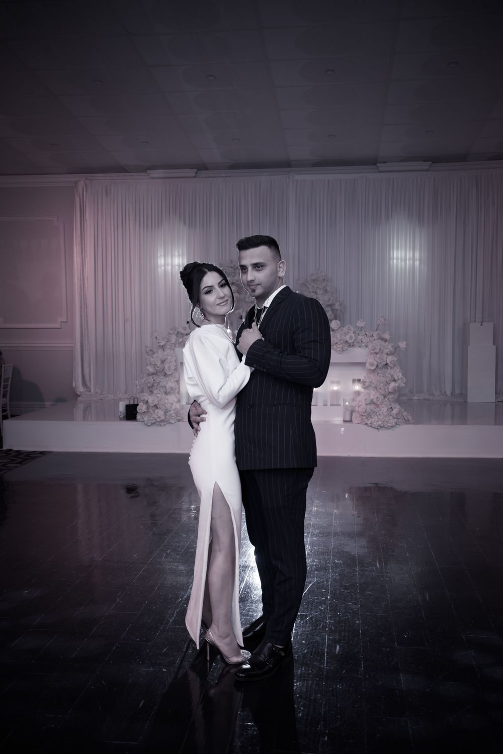 Couple shares romantic dance moment on dark reflective ballroom floor.