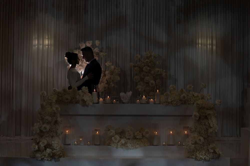 A couple's silhouette framed by candlelit floral arch during evening reception.
