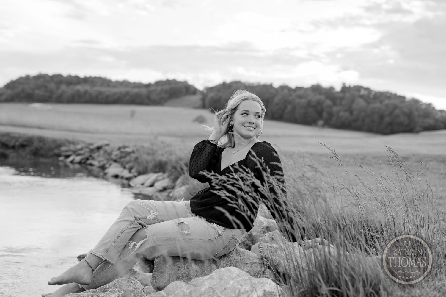 Black and white portrait of someone relaxing on rocks near a lake at golden hour.