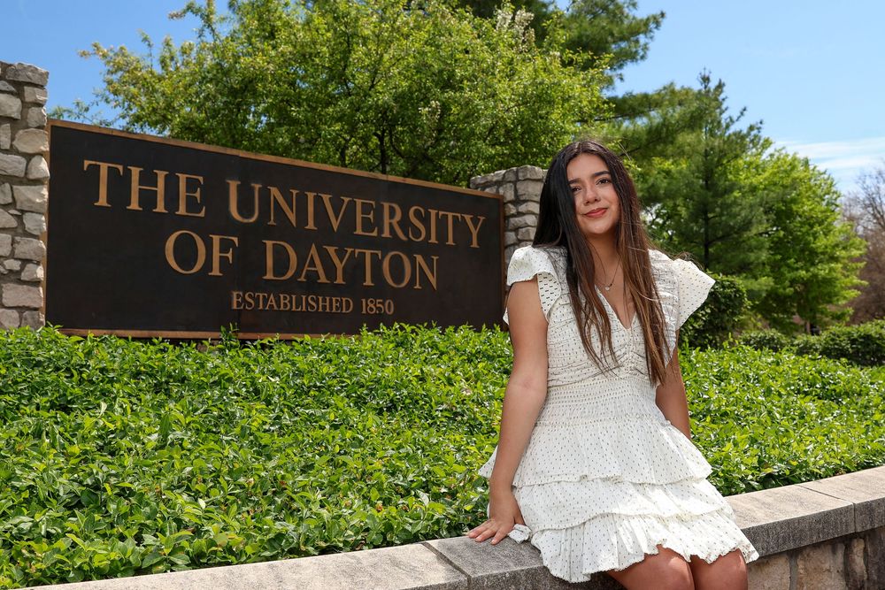 Graduate posing by University of Dayton entrance sign during spring commencement.