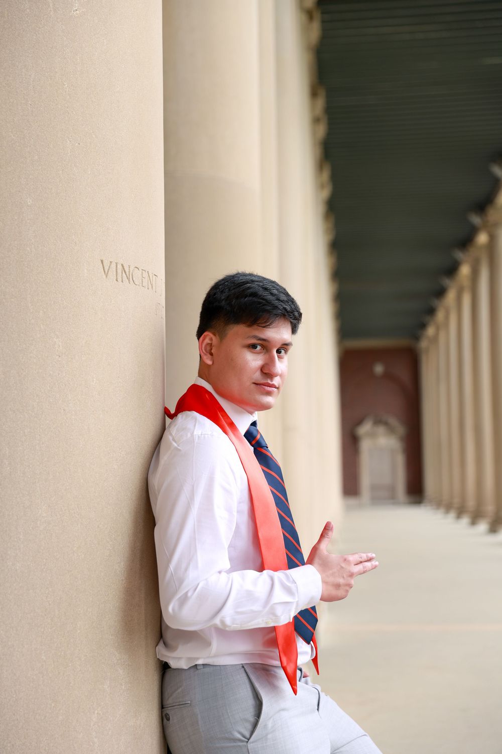 A graduate in formal attire poses against white columns in a classical architectural setting.