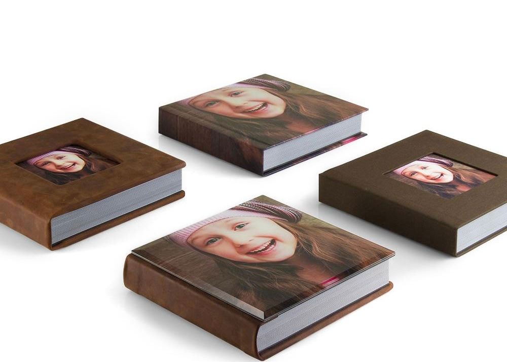 Four brown leather photo books with portrait window covers displayed on white background.