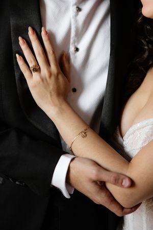 Close-up view of a couple's hands embracing, with bride in white lace and groom in black formal attire.