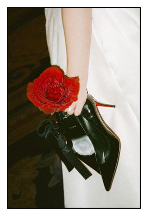 A single red rose held next to a black high heel shoe against a dark background with white fabric.