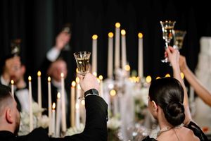 Wedding guests raise champagne glasses in a toast during an elegant candlelit reception celebration.