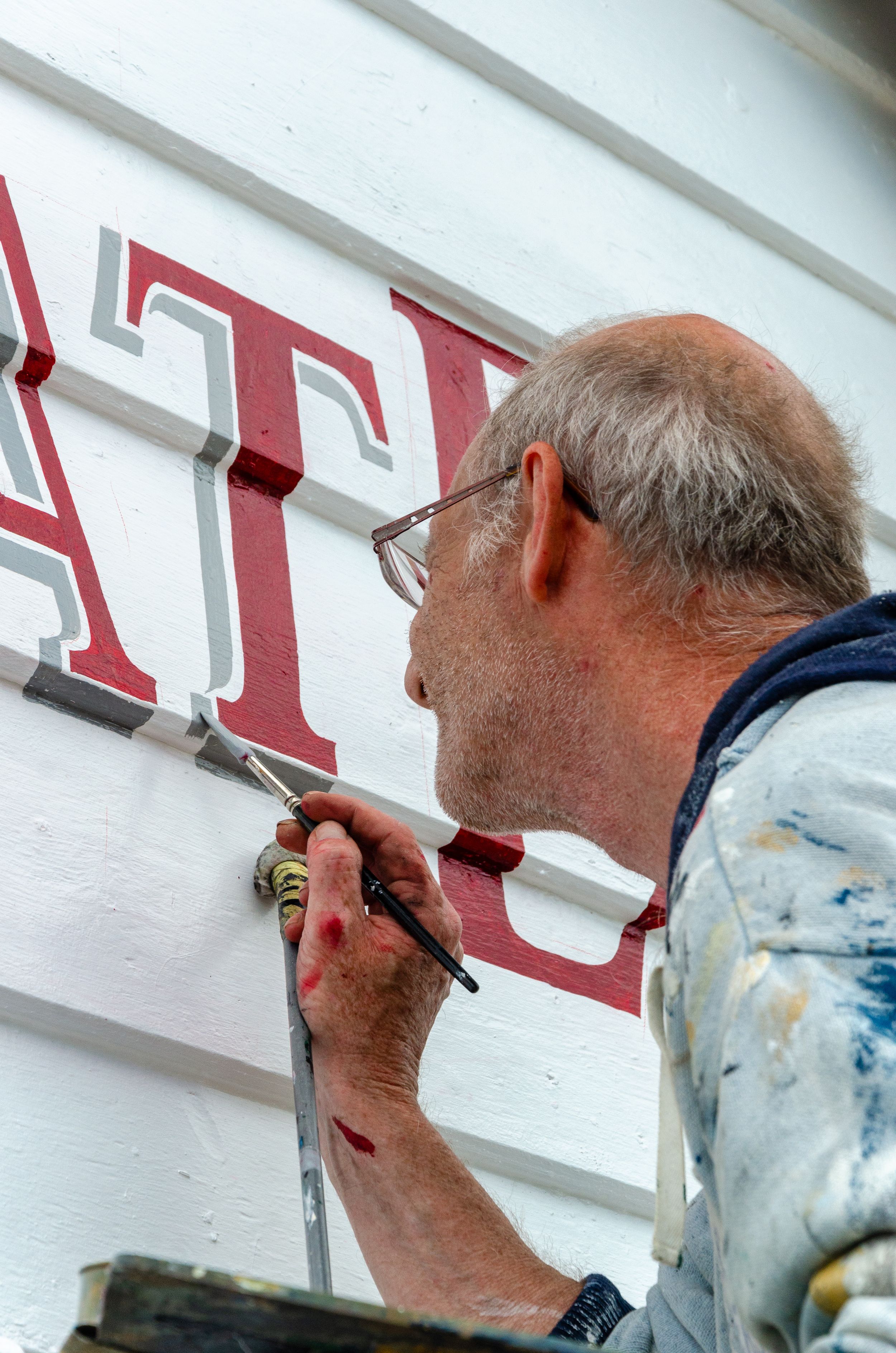 Close up of someone painting red lettering on a white building wall.
