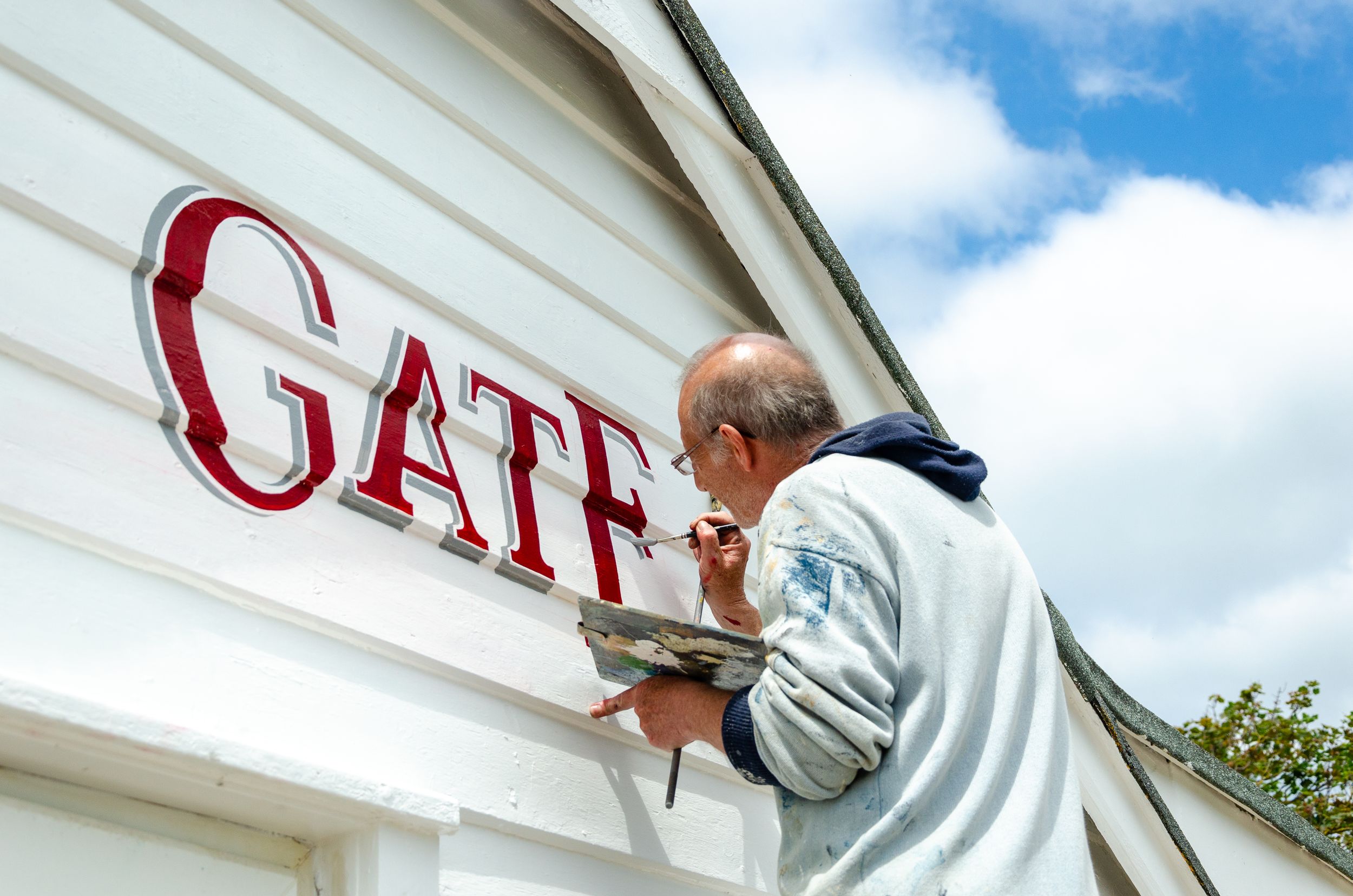 Close-up view of hand painting red lettering on white building wall.