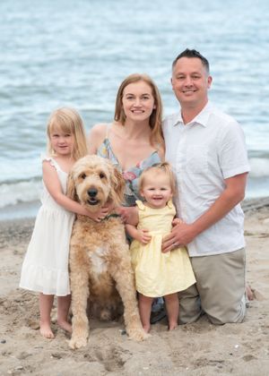 Beach family portrait with goldendoodle dog at water's edge.