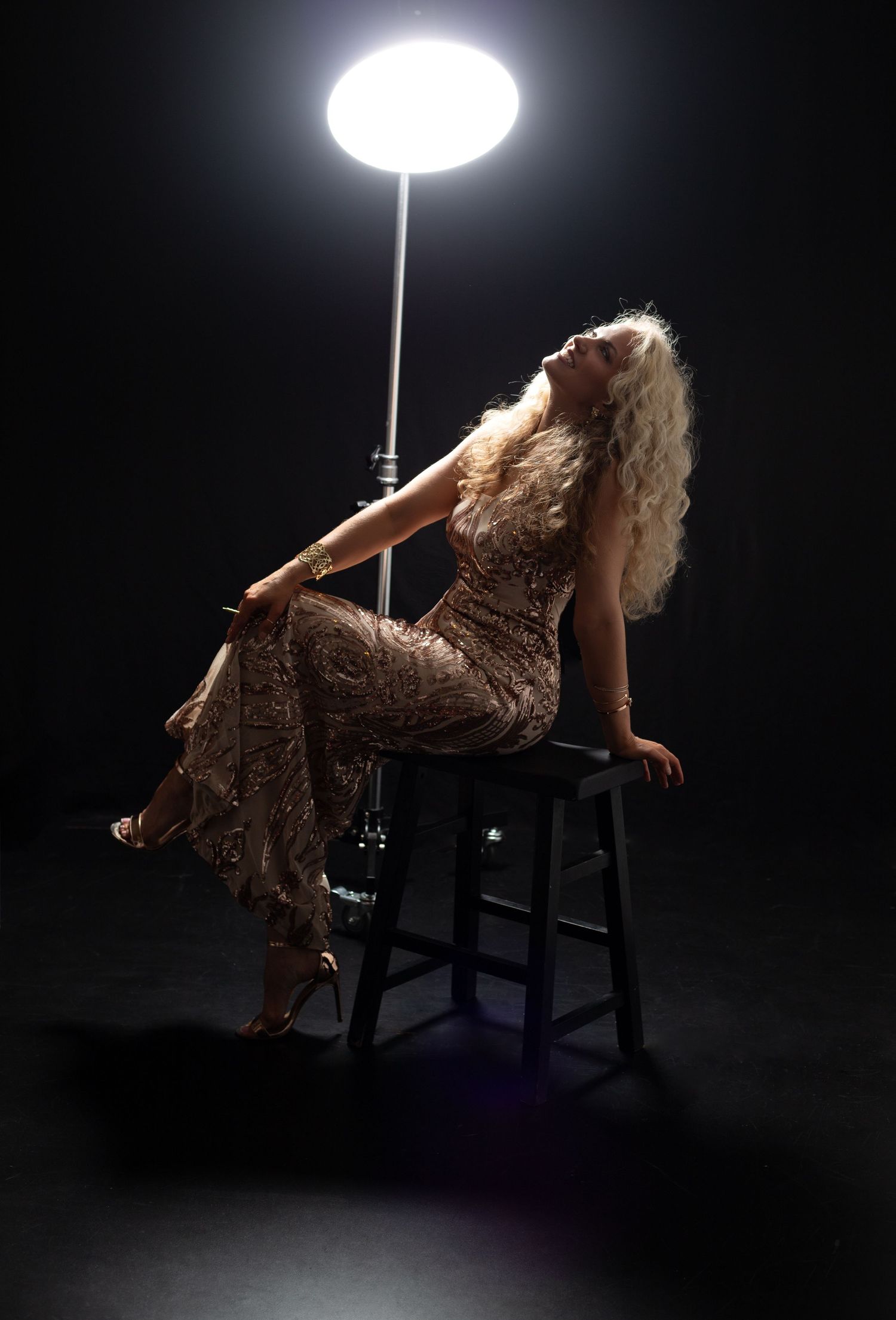 Dramatic silhouette of a women with flowing long hair in a sequined dress posing on a chair against a dark background with spotlight.
