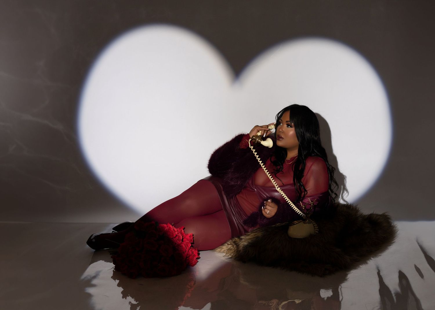 A dark silhouette of a women posing in an expressive position on a phone prop in front of a heart-shaped light background.
