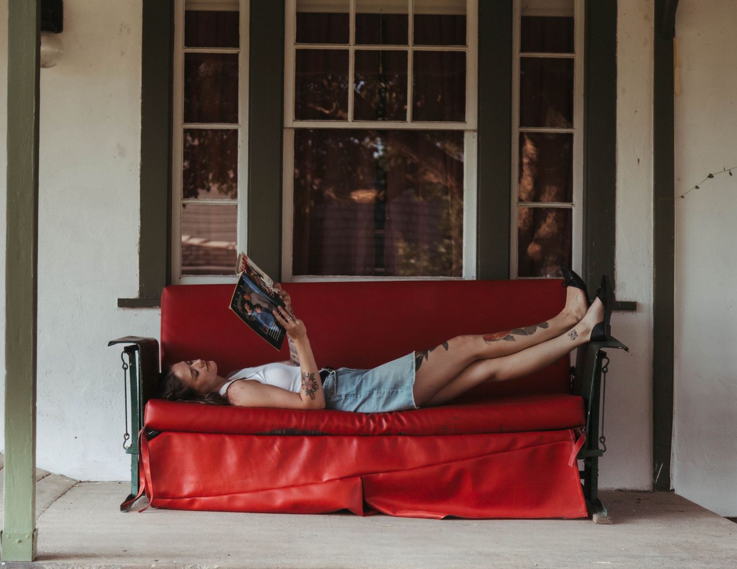 Person relaxing on a bright red porch swing outside a house with white columns.