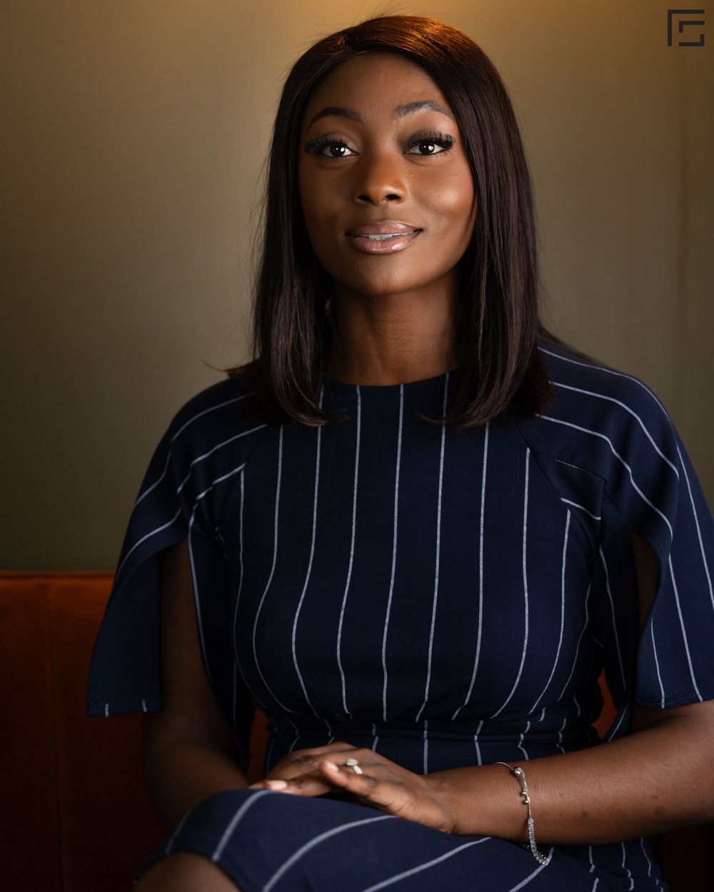 Professional portrait of someone wearing a navy pinstriped dress sitting in front of a neutral brown background.