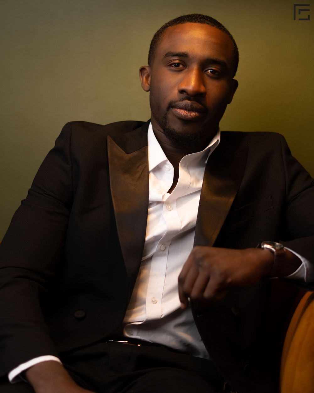 Professional portrait photo showing person in dark blazer and white dress shirt seated against neutral background.