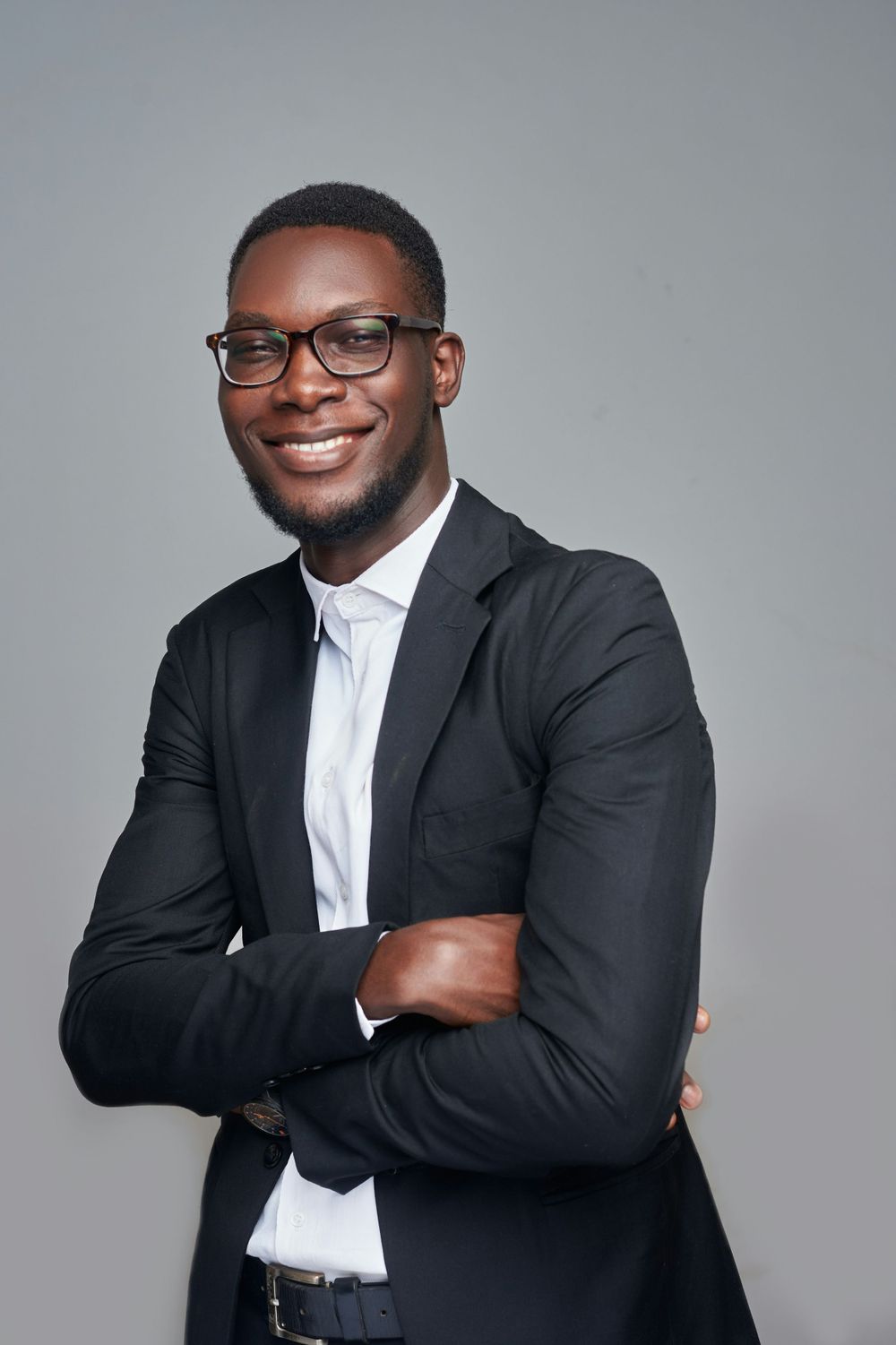 Professional studio portrait of person wearing glasses and dark suit with arms crossed.