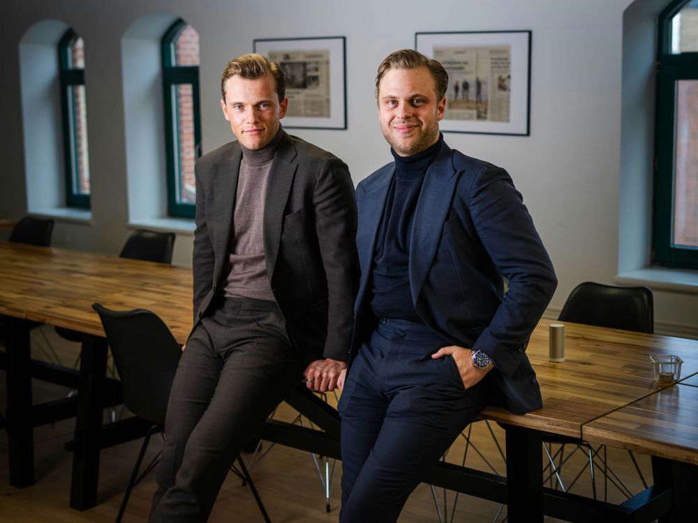 Two business professionals in suits sitting casually in a modern office space.