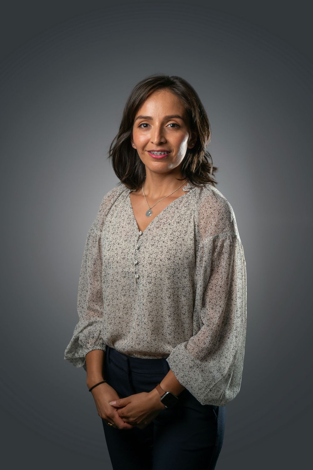 Studio portrait of a person in a patterned blouse against a gray background.