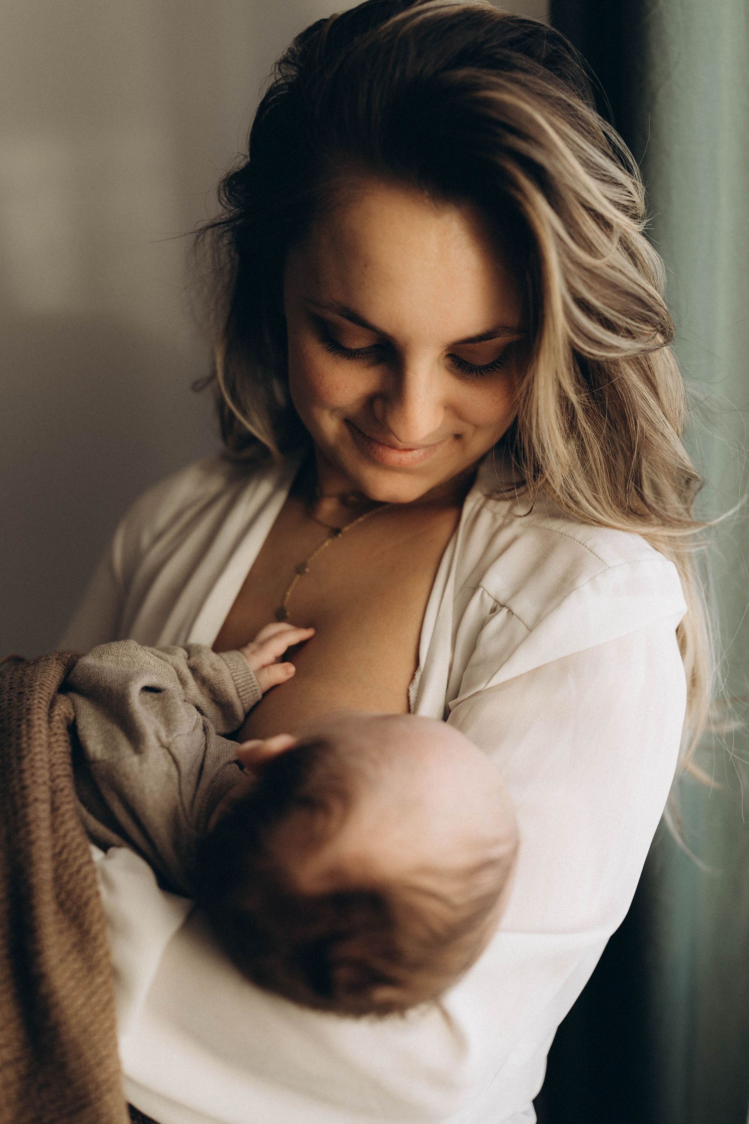 An intimate moment of mother nursing her newborn baby in moody lighting.