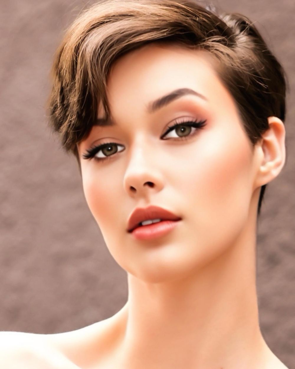 Beauty portrait with short brown hair and glamorous makeup against neutral background.