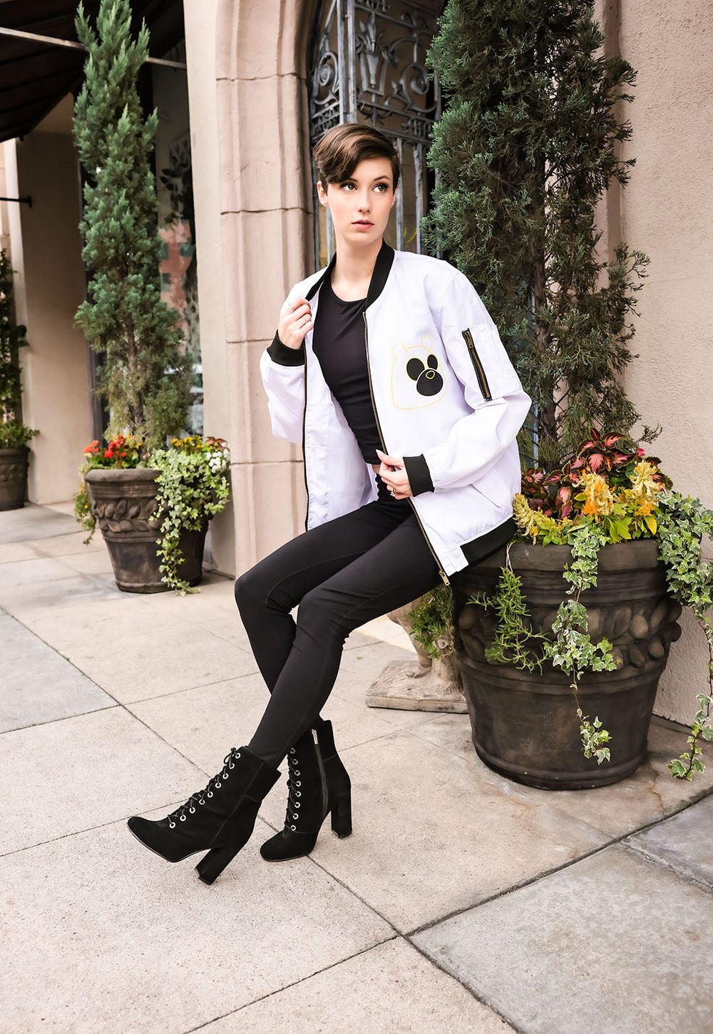 Fashion model in white jacket and black leggings poses near decorative planters.