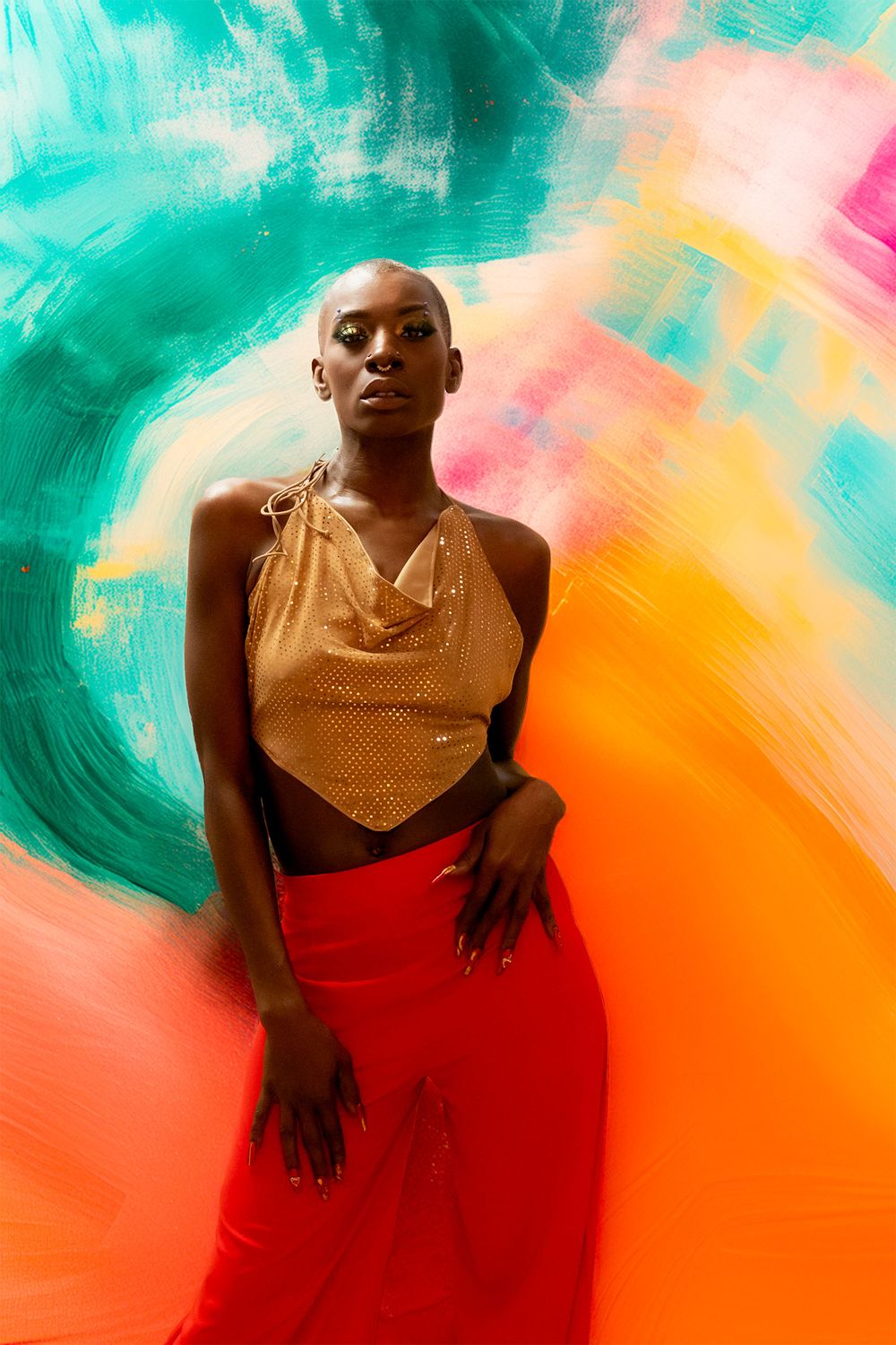 Artistic portrait against vibrant turquoise and orange background wearing gold top and red skirt.