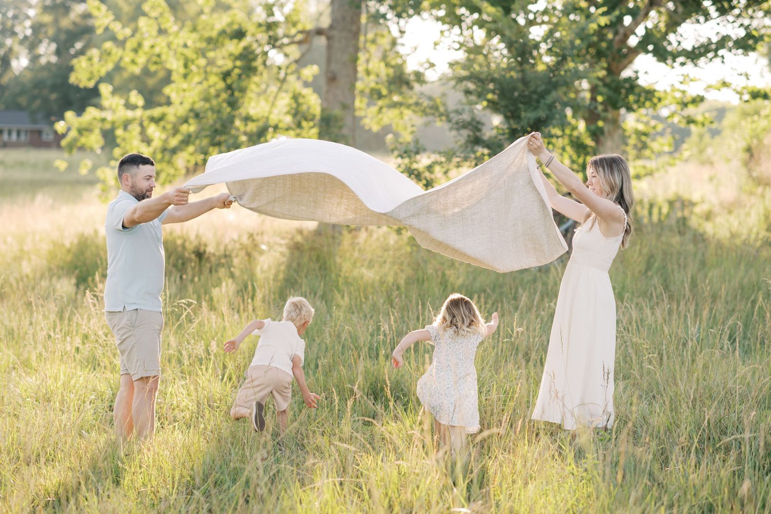 Family with baby standing in a lush green meadow beside a calm pond.