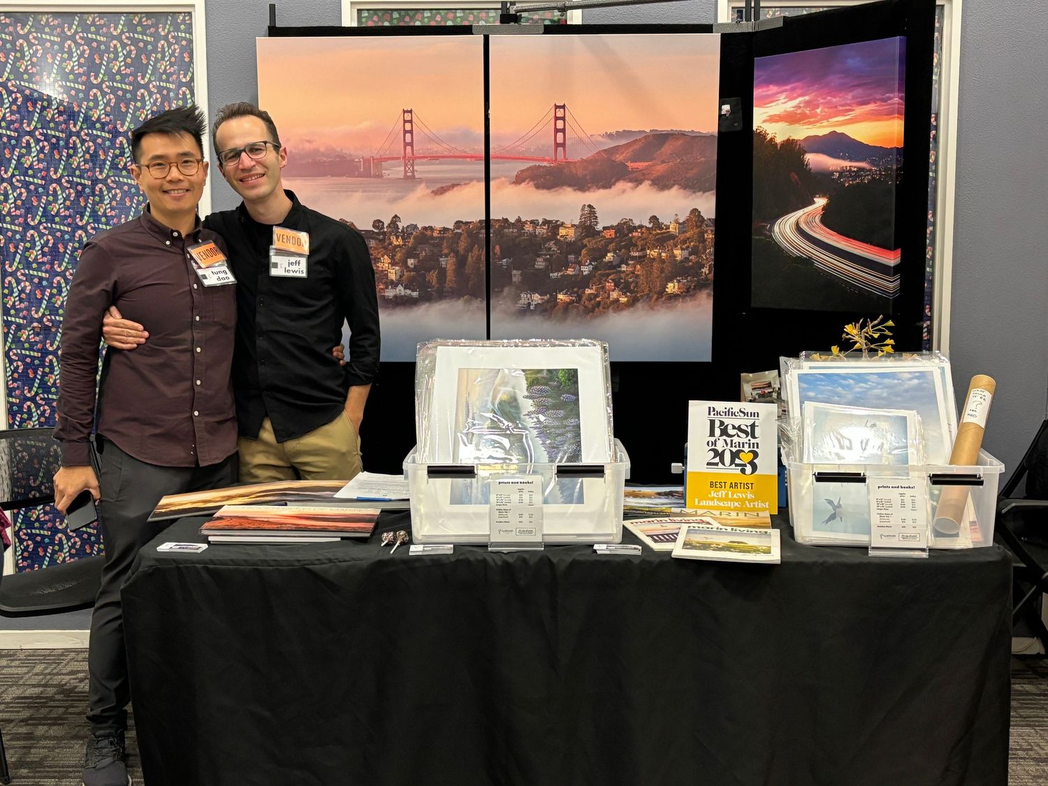 Photography booth display showcasing landscape prints and Golden Gate Bridge imagery on a black table.