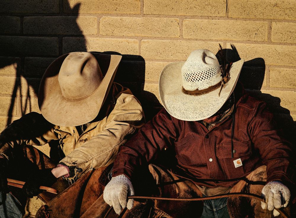Two people in cowboy hats and western attire seated together in a dim-lit setting.