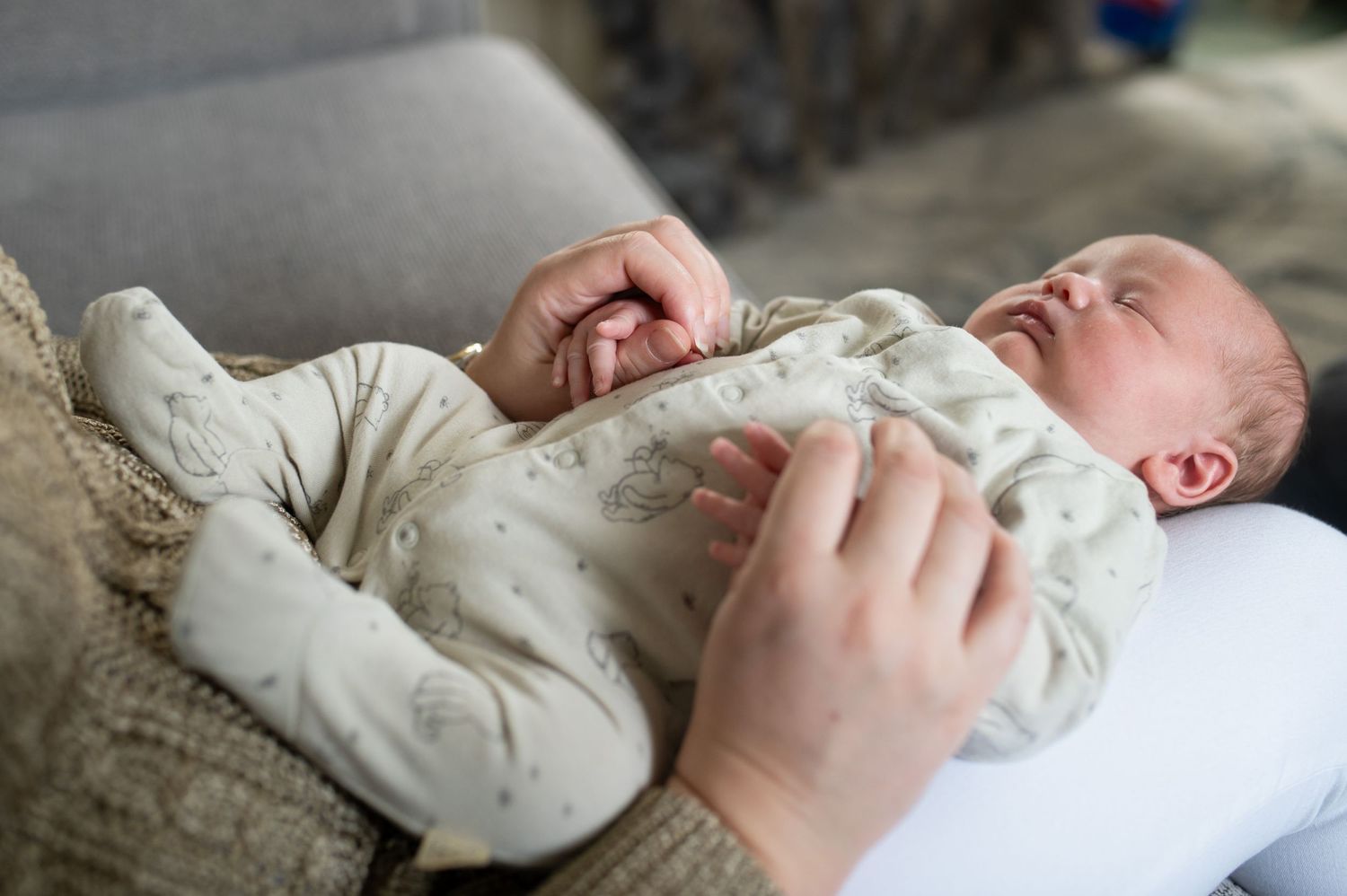 Newborn lying on his mum's lap, whilst she holds his hands in hers. Sarah Frame Photography, Newborn photographer Surrey