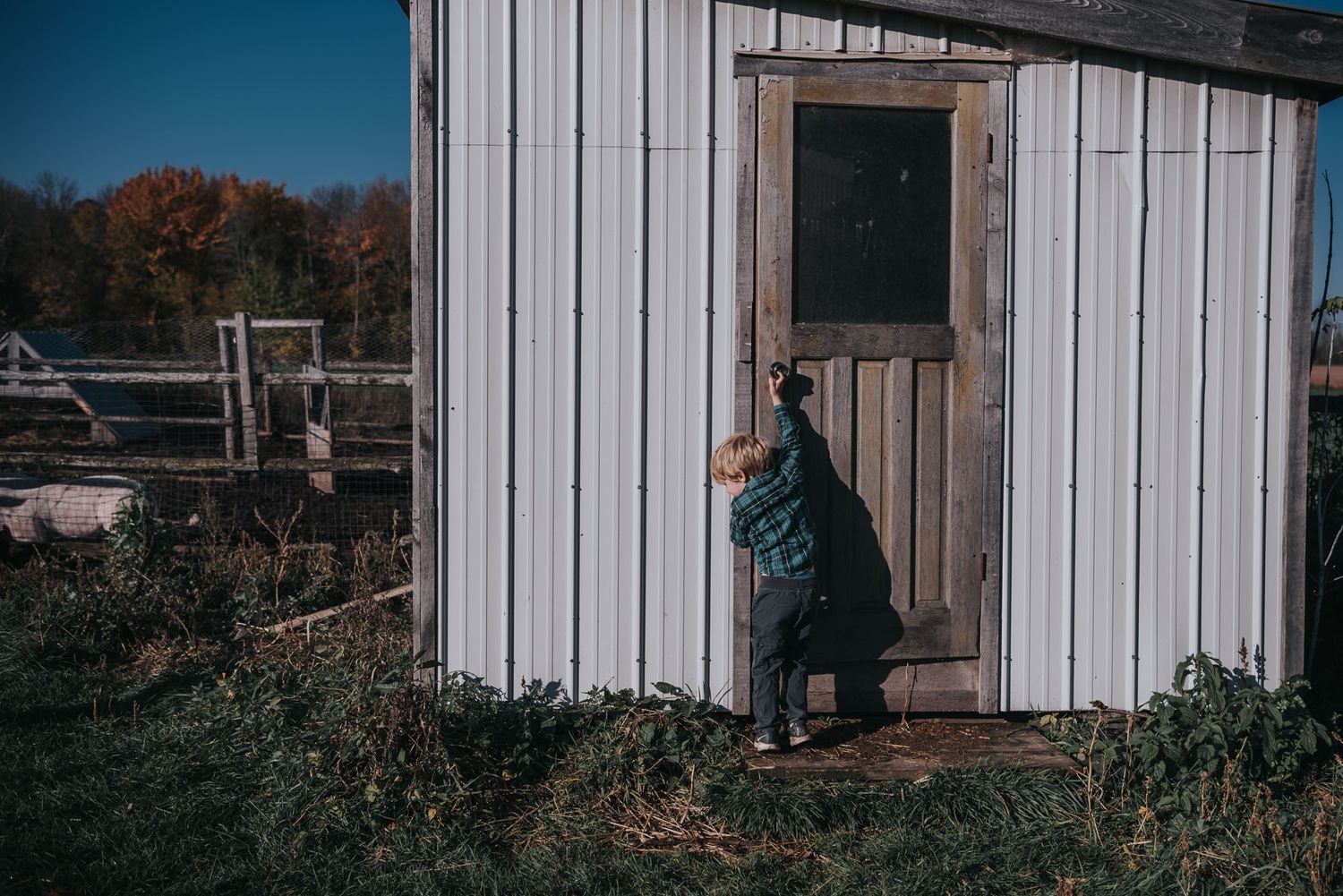 A young boy reaches to open a door on a white building.