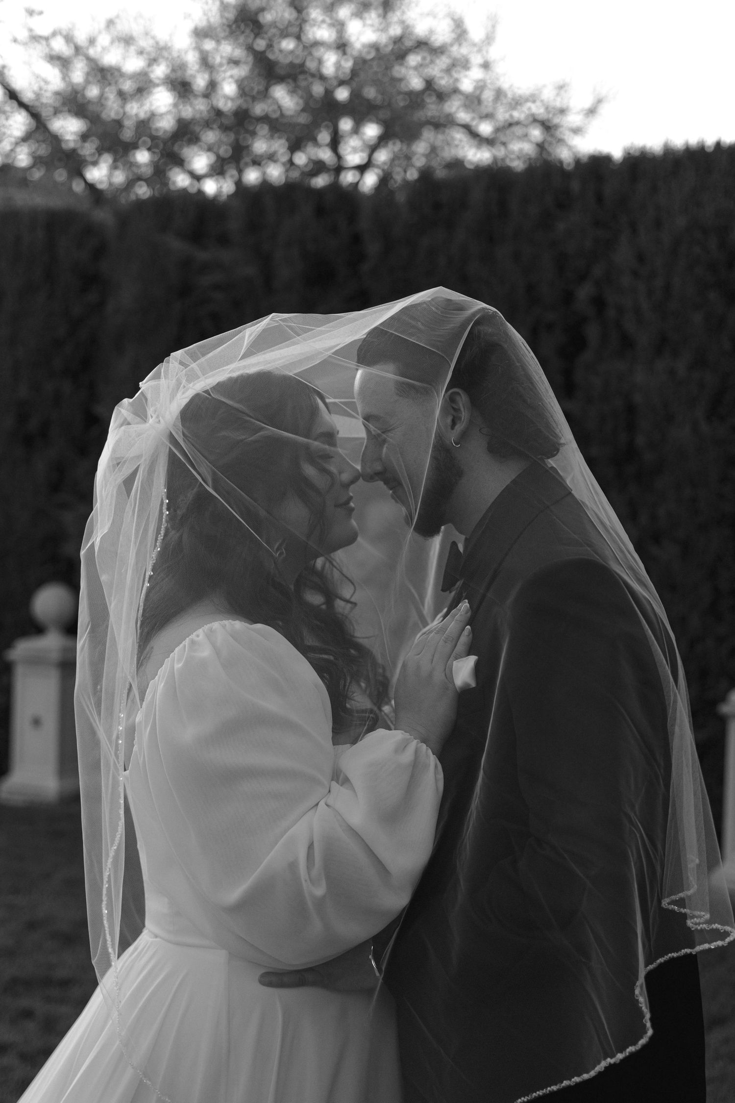 A romantic black and white portrait of a bride and groom sharing an intimate moment under a veil.