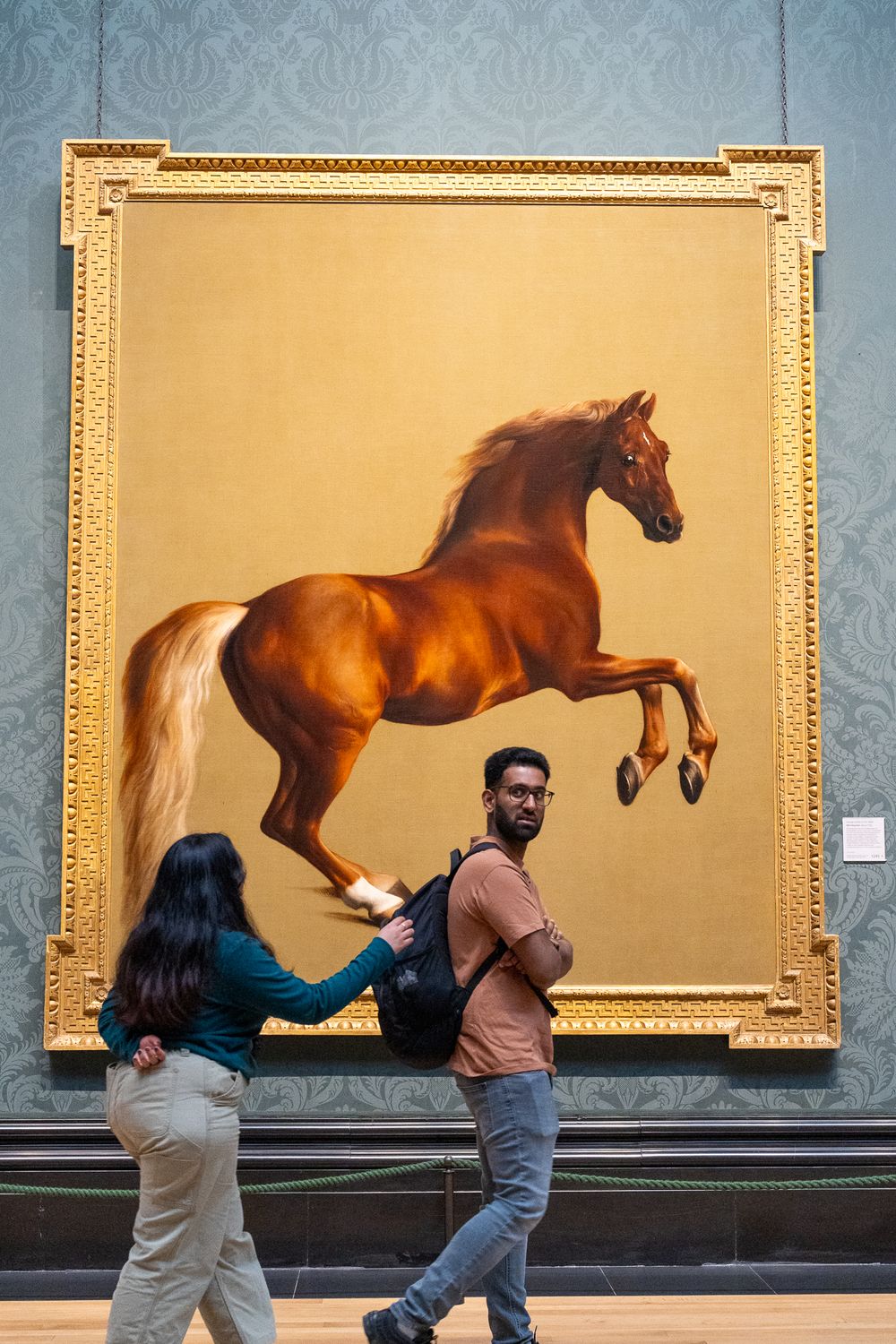 Large painting of a rearing brown horse in an ornate gold frame at an art gallery.