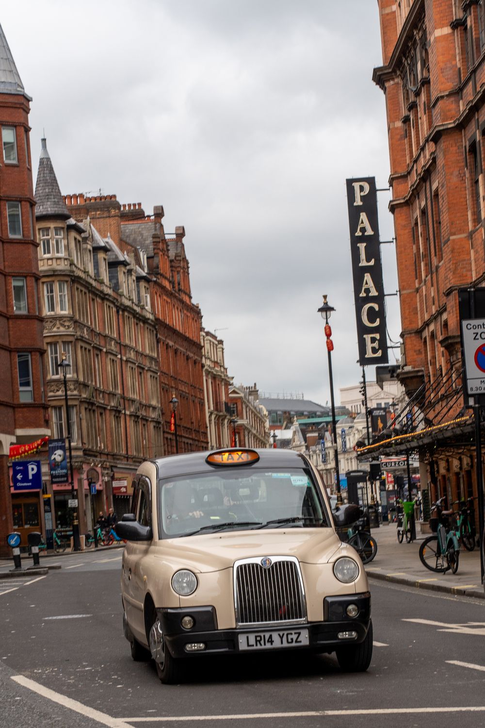 Classic London taxi cab drives past historic red brick buildings with Palace sign.