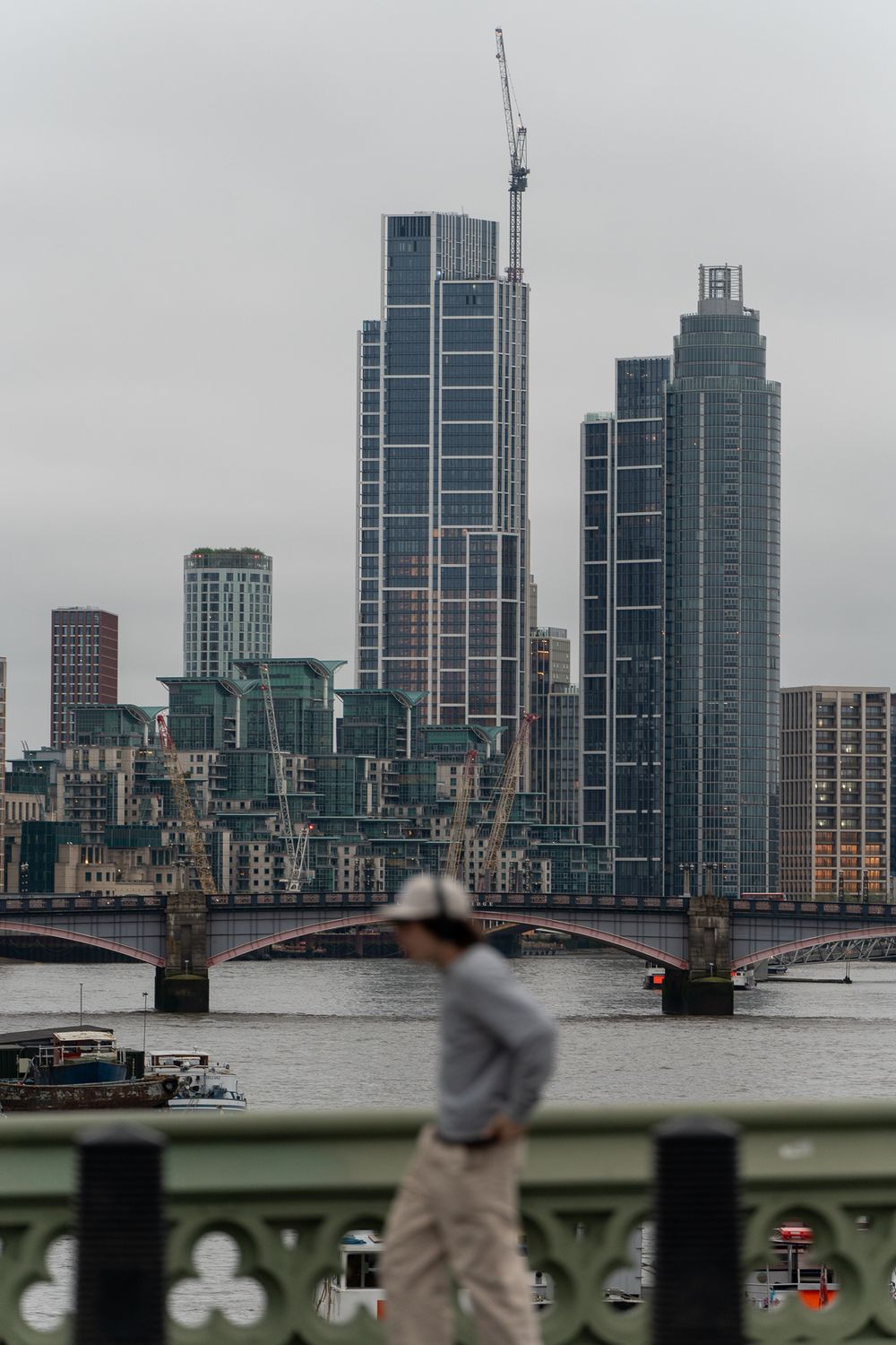 Modern skyscrapers and construction cranes along London's Thames River on an overcast day.
