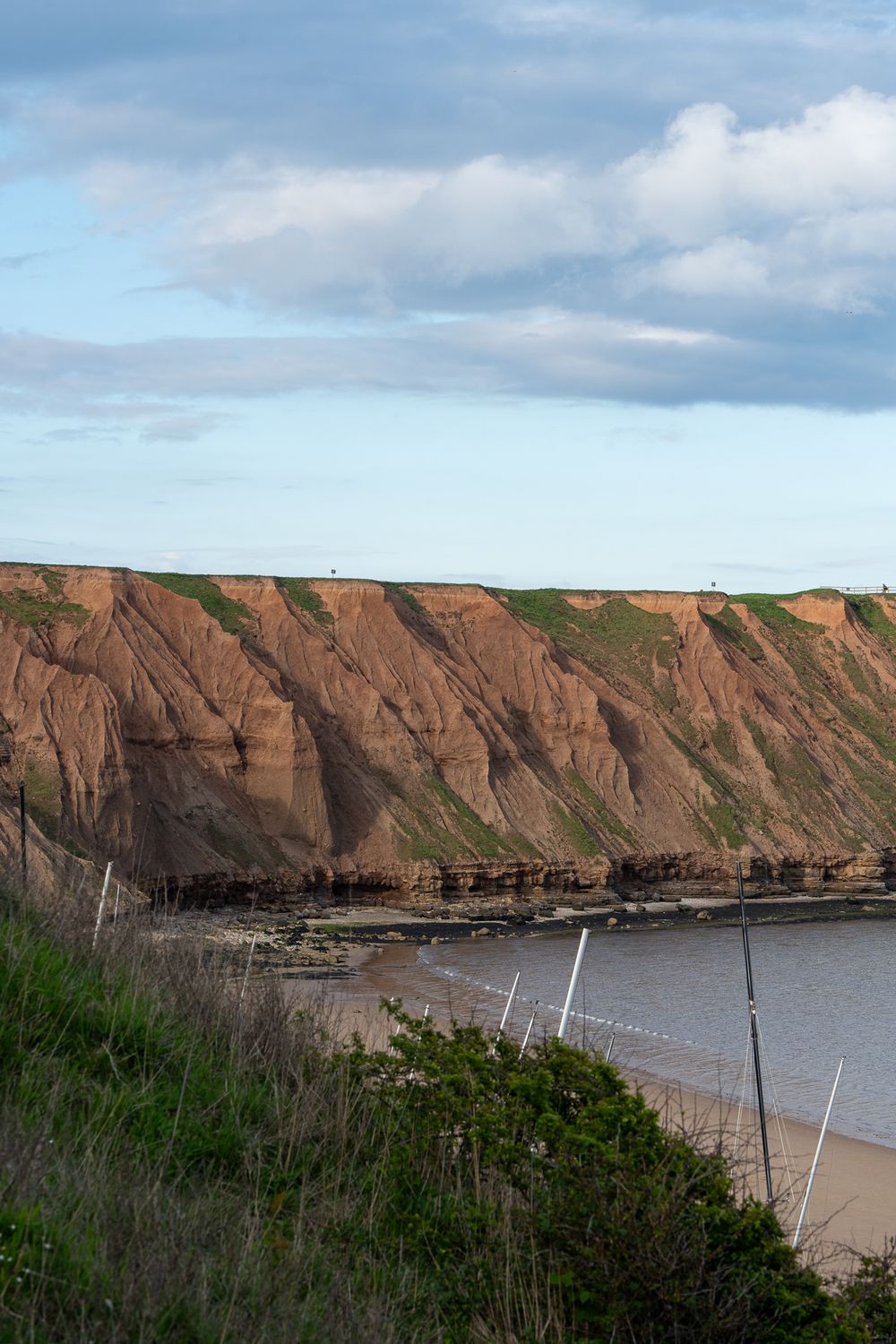 Rugged coastal cliffs with reddish-brown layers rise above a secluded beach.