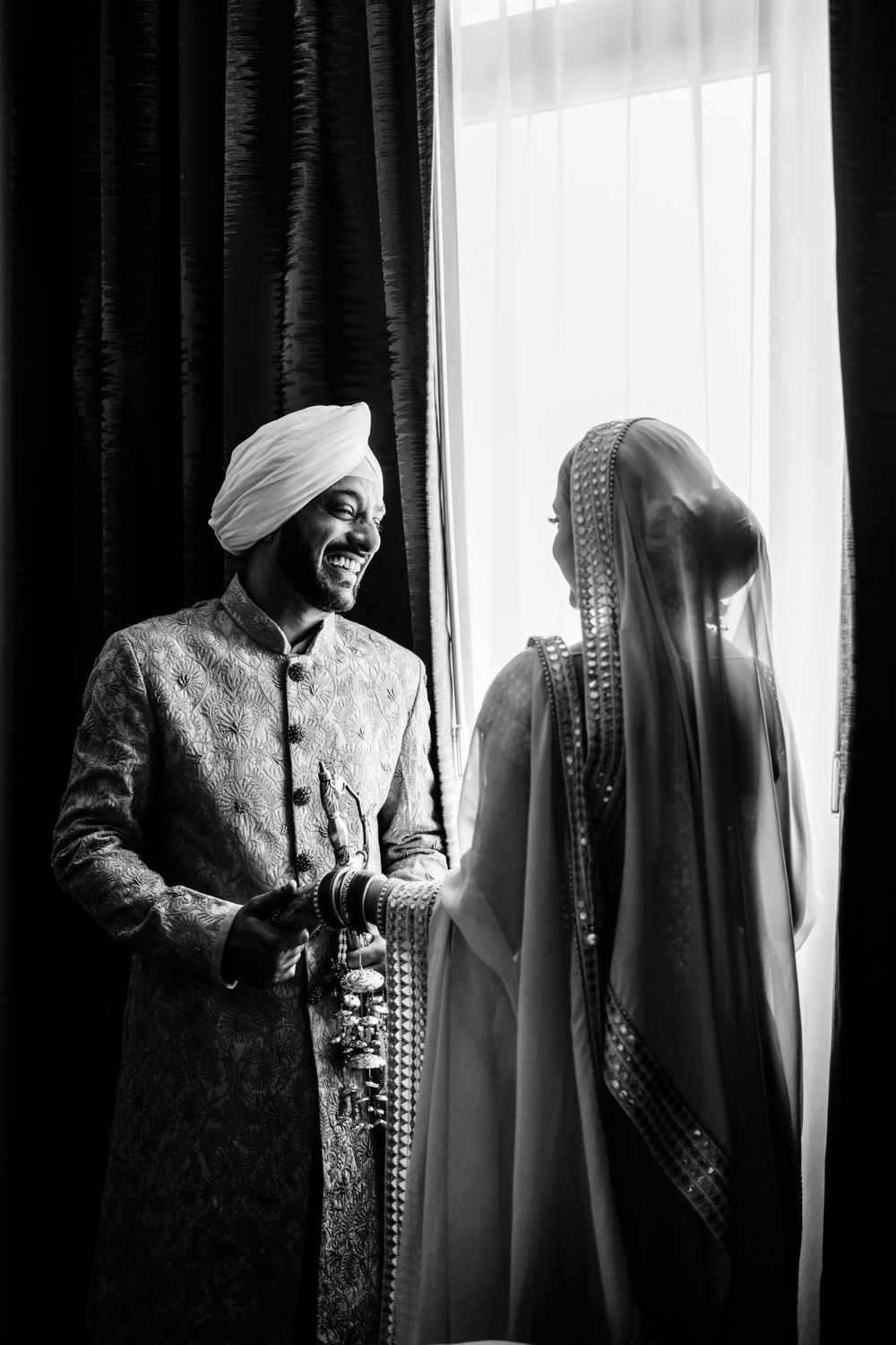 Black and white portrait of Sikh couple sharing an intimate moment by a window.