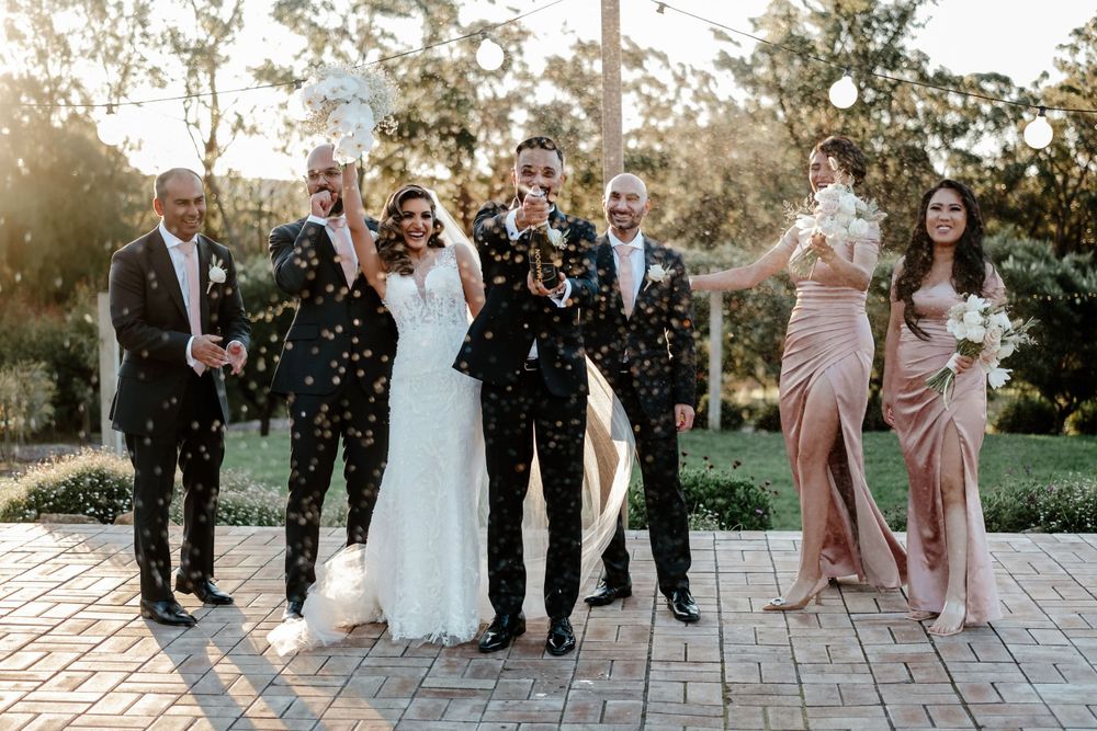 Wedding party celebrating with confetti on brick paved pathway.