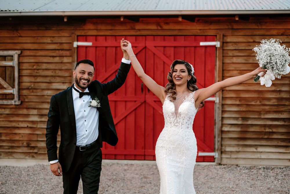 Celebratory pose of newlyweds in front of rustic red barn door.