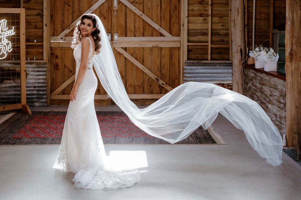 A flowing white wedding dress and veil captured in a rustic barn setting with dramatic lighting.