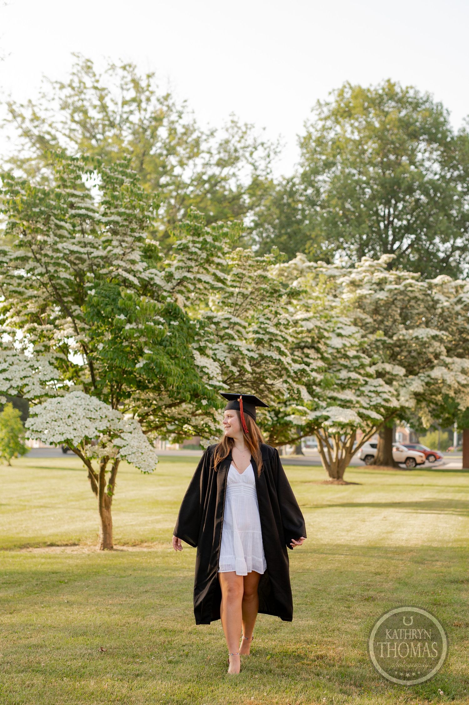 Graduation photo showcasing academic regalia against flowering trees on a sunny campus lawn.